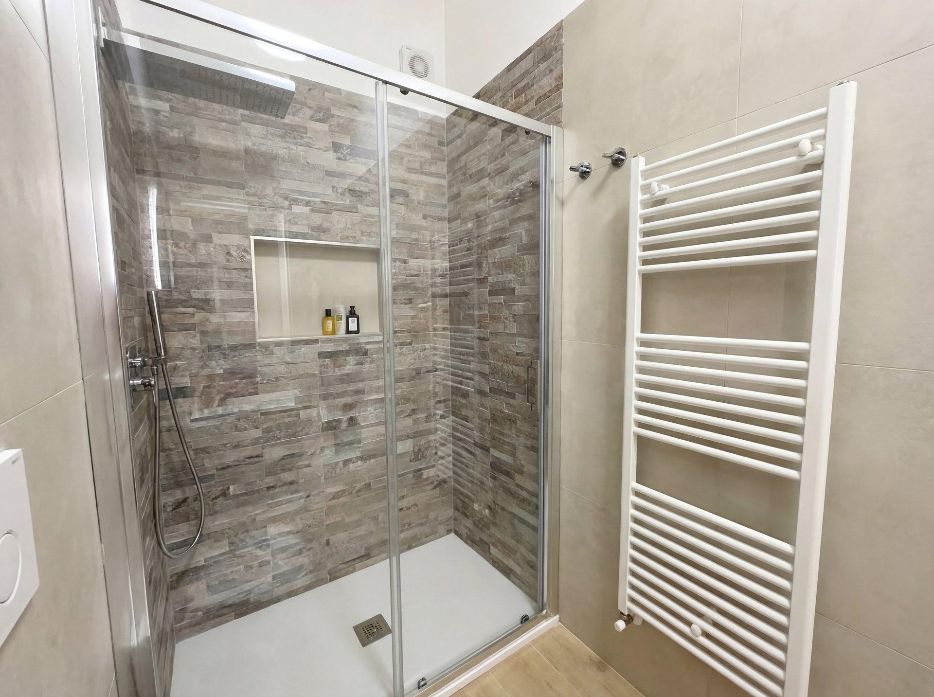 Walk-in rainfall shower with natural stone tiles and glass partition in Terra apartment bathroom