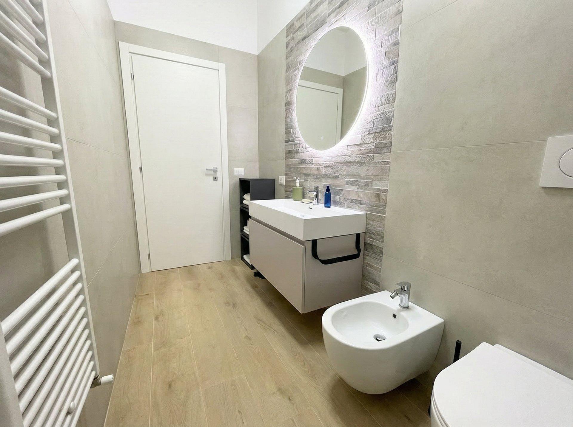 Bathroom detail with oval mirror, modern vanity, and Acqua di Parma amenities in Sunset Garden Terra